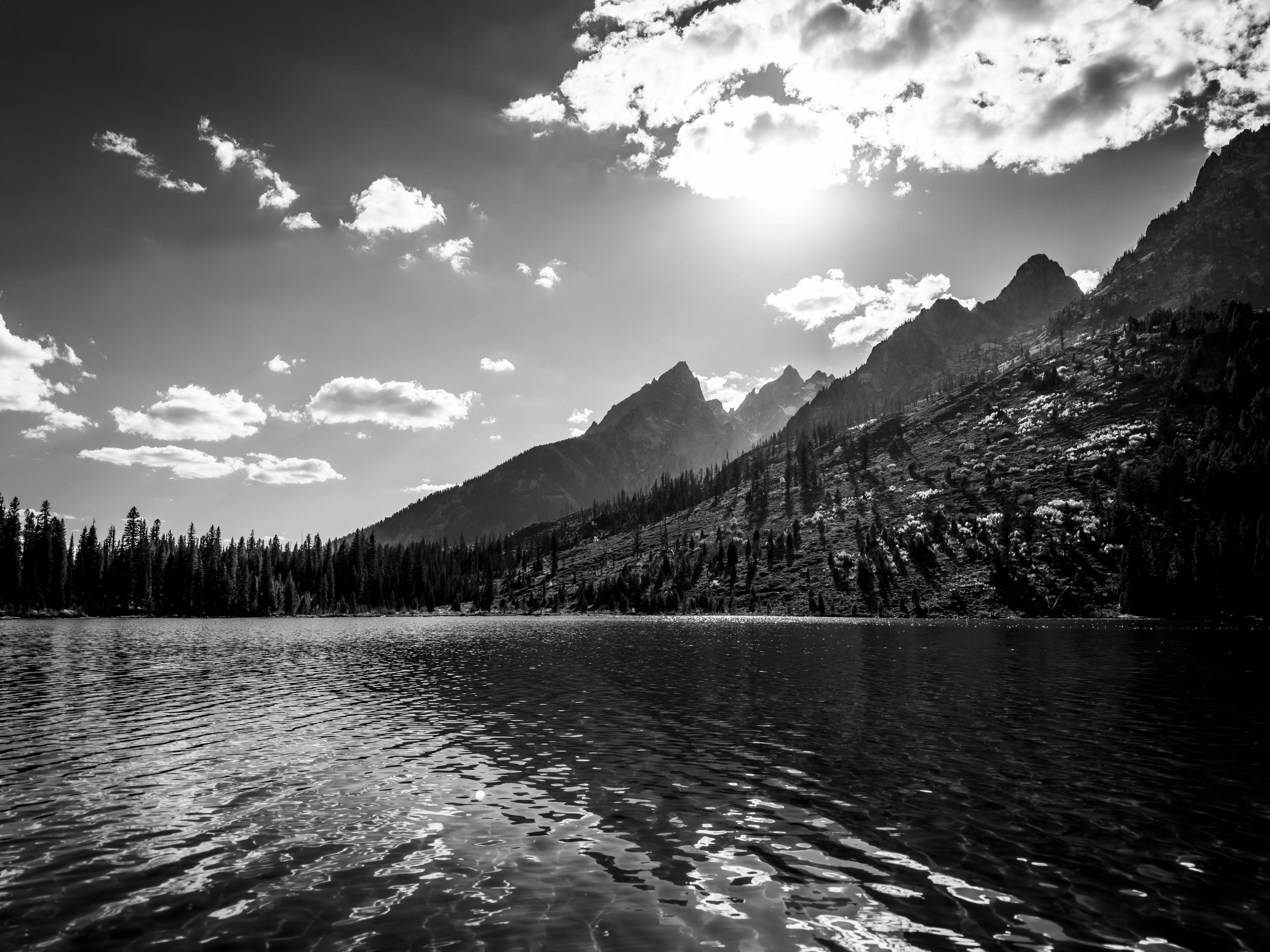 The Teton Range, including Teewinot Mountain, Grand Teton, and Mount Owen, seen backlit by the Sun, from the surface of String Lake.