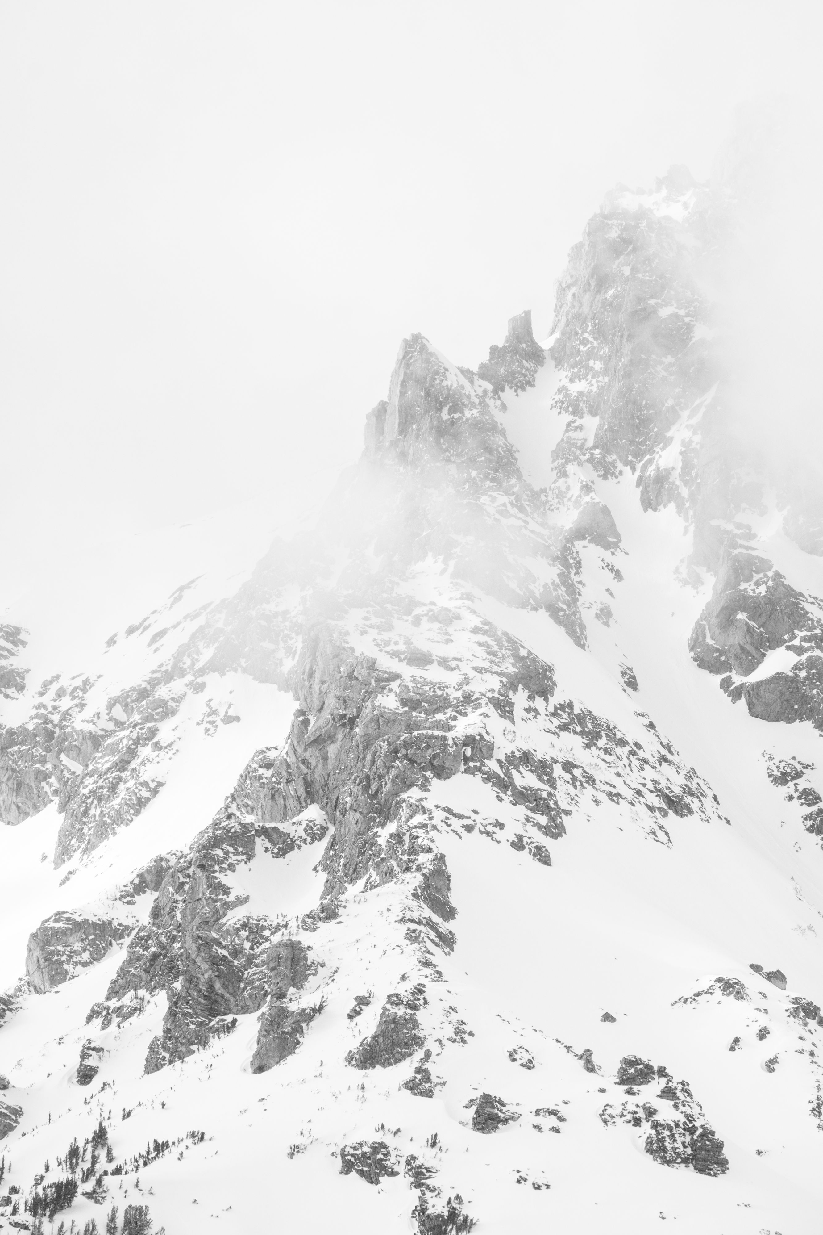 A close-up of a snow-covered peak in the Tetons, surrounded by clouds.