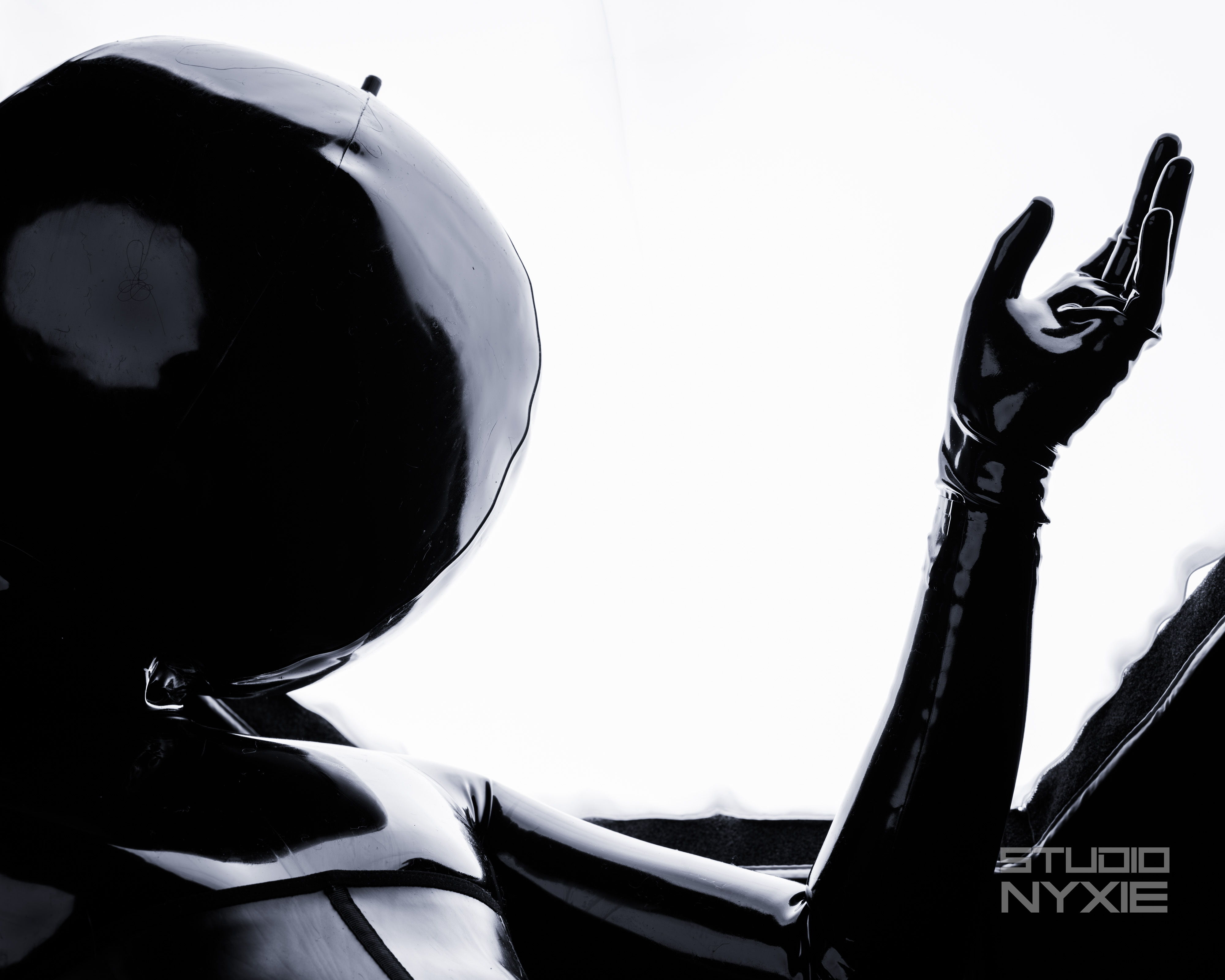 A latex clad figure in a inflatable ball hood and latex suit is backlit by an octagonal diffuser from a photography light
